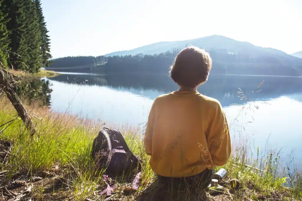 A woman in a yellow sweater sitting by a lake, looking out at the hills. Counseling for adults near Tigard, Oregon.