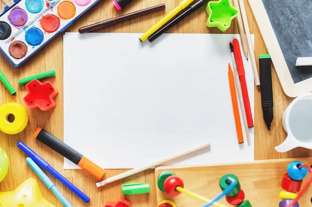 Paints, markers and crayons around a blank sheet of paper on a wooden table. Child and teen therapy near Tigard, Oregon.