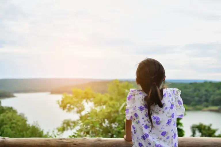 A child seen from behind, looking out over a lake from a wooden rail. Therapy for third culture kids and multicultural families.