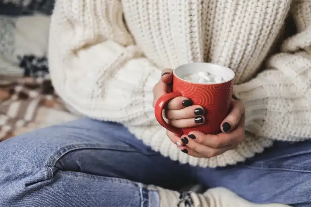Hands holding a red mug of cocoa, in a knitted sweater. Telehealth counseling anywhere in Oregon.
