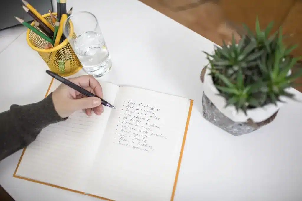 A hand writing in a notebook beside a potted plant. Cognitive Processing Therapy (CPT) near Tigard, Oregon.
