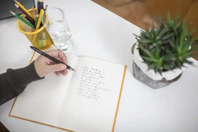 A hand writing in a notebook beside a potted plant. Counseling for adults near Tigard, Oregon.