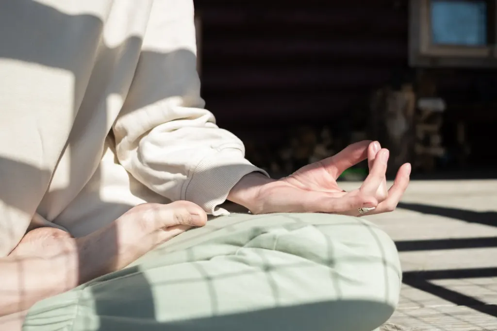 Hands resting on the knees in a meditation pose, in sunlight. Somatic trauma therapy near Tigard, Oregon.