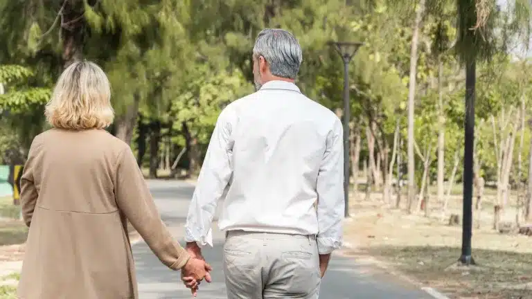 An older couple walking hand in hand through a park, seen from behind. Counseling for adults near Tigard, Oregon.