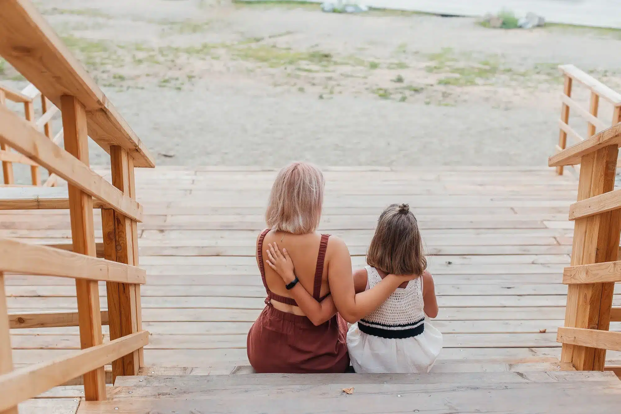 A parent and child sitting side by side on wooden steps, seen from behind. Talking to your child about therapy, from a counselor near Tigard, Oregon.