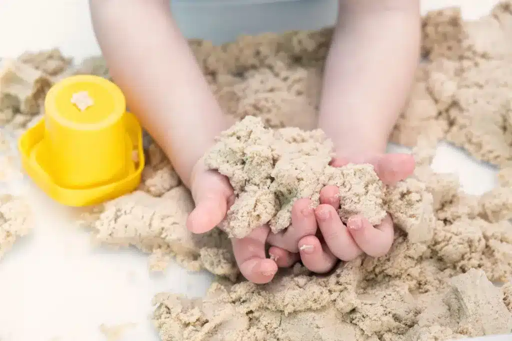 Hands holding sand beside a yellow toy bucket. Child and teen therapy near Tigard, Oregon.
