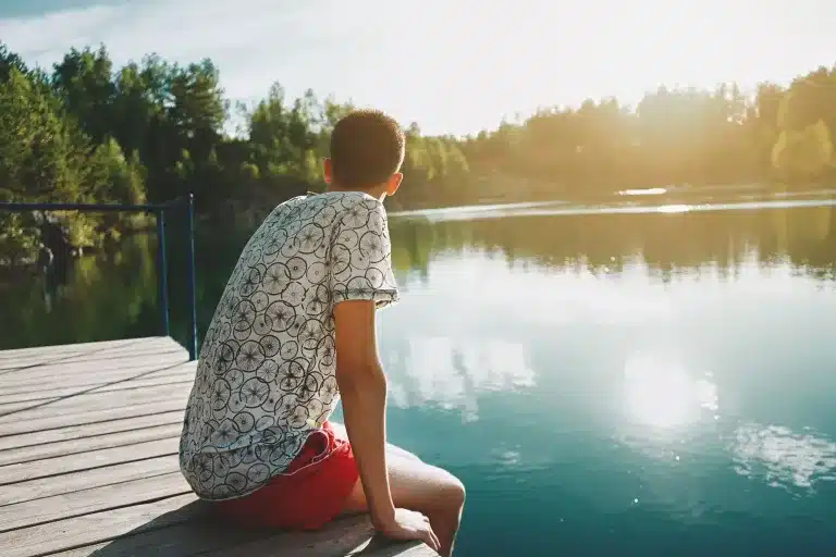 A teenager sitting on a dock by a lake, seen from behind. Child and teen therapy near Tigard, Oregon.