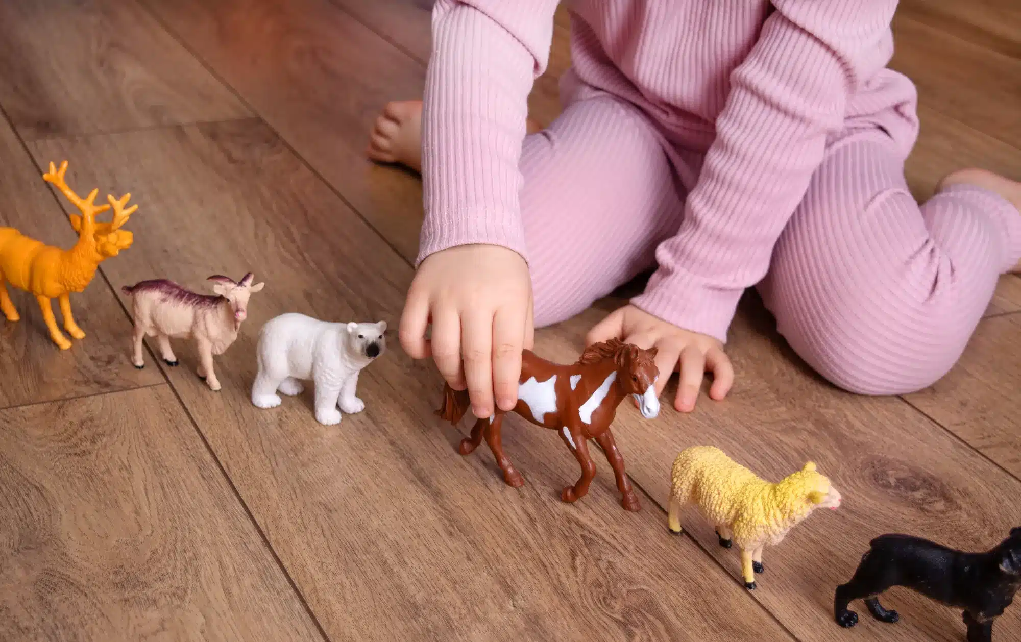 A child's hand moving toy animals across a wooden floor. How play therapy works, from a counselor near Tigard, Oregon.